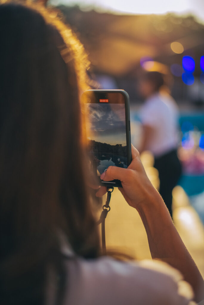 Selective focus on modern cellular phone using for clicking pictures via camera, millennial woman tourist taking photos or shooting video via mobile phone during evening walk