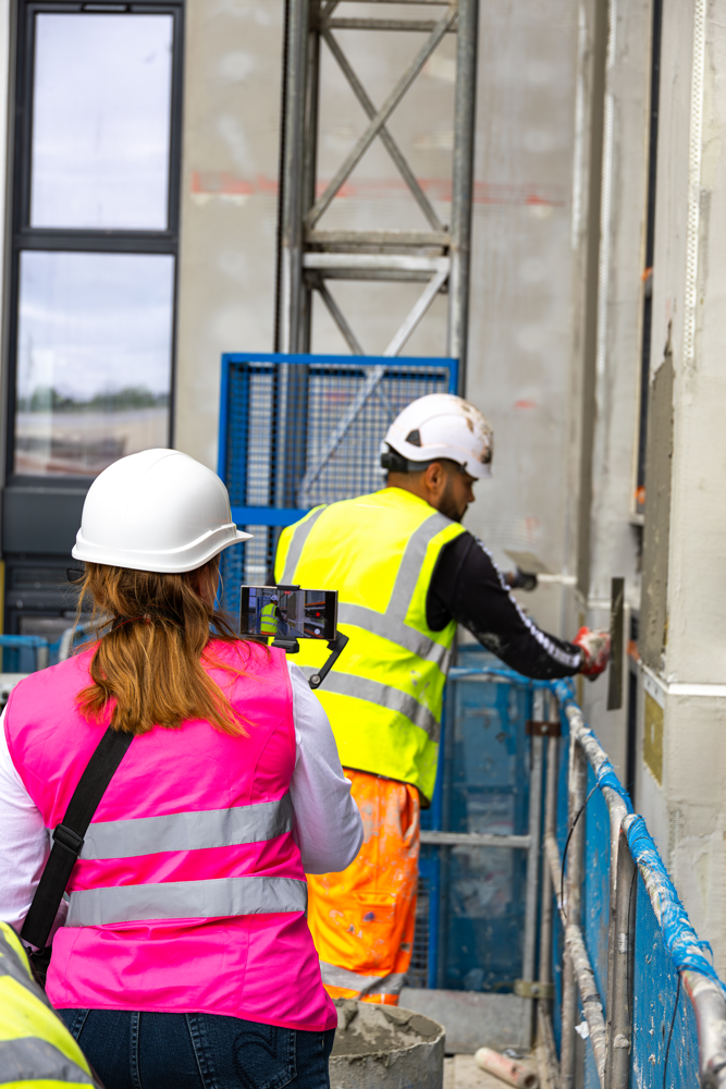 A Big Reputation team member filming on a phone while a worker renders a wall on a construction site